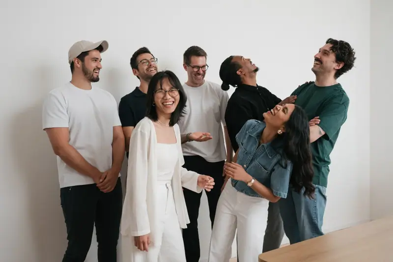 A diverse group of colleagues standing together and laughing in a bright office setting.