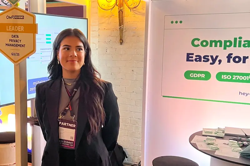 A colleague standing at a heyData booth during an event, with compliance information displayed in the background.