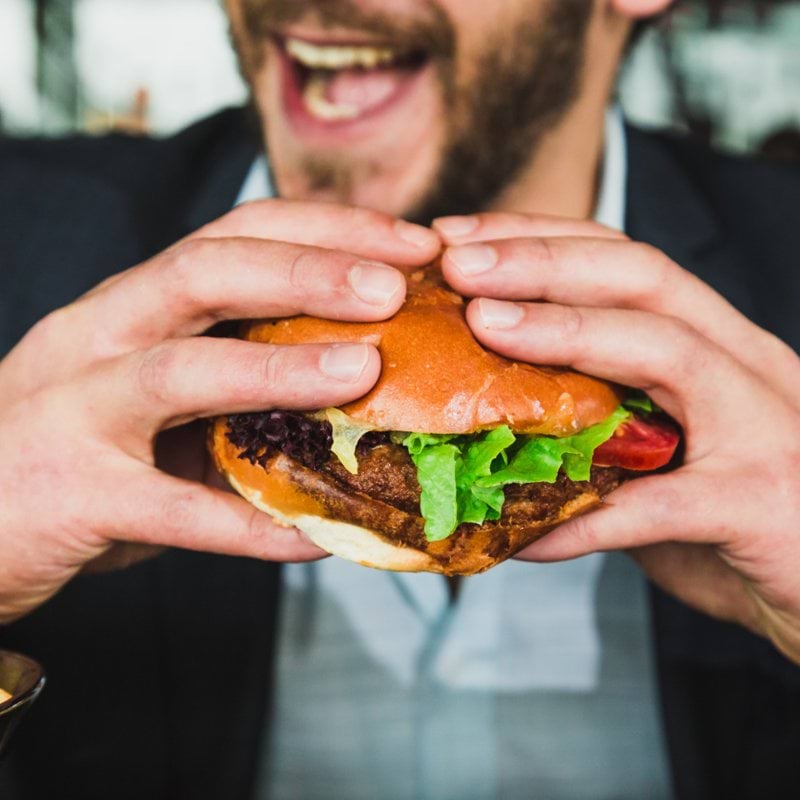 person holding burger bun with vegetables and meat