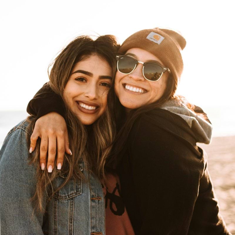 woman hugging other woman while smiling at beach