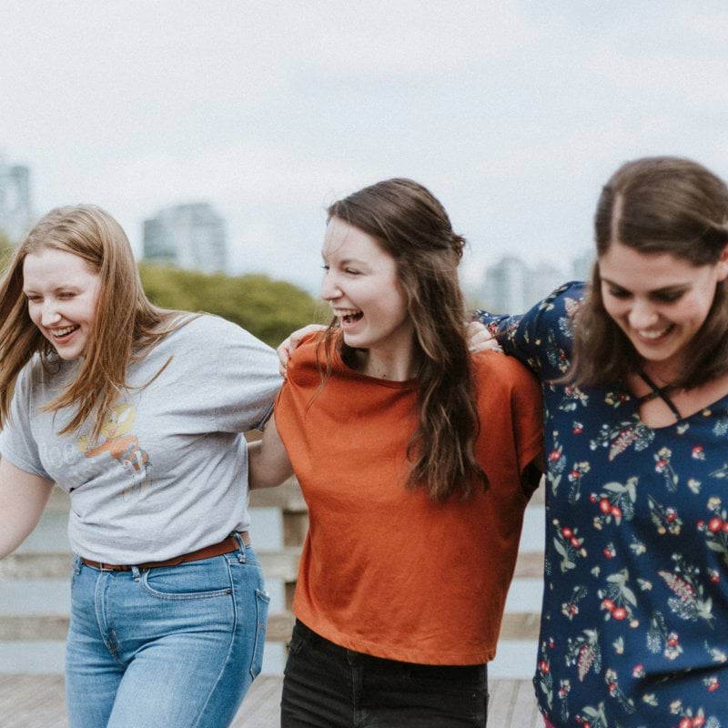 three women walking on brown wooden dock near high rise building during daytime
