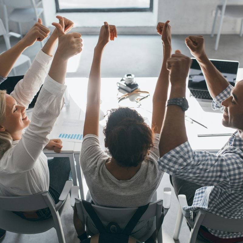 a group of people sitting at a table raising their hands