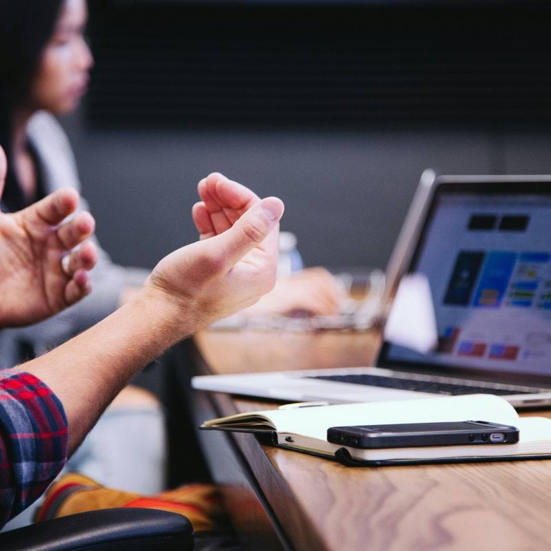 person gesturing during meeting with laptop