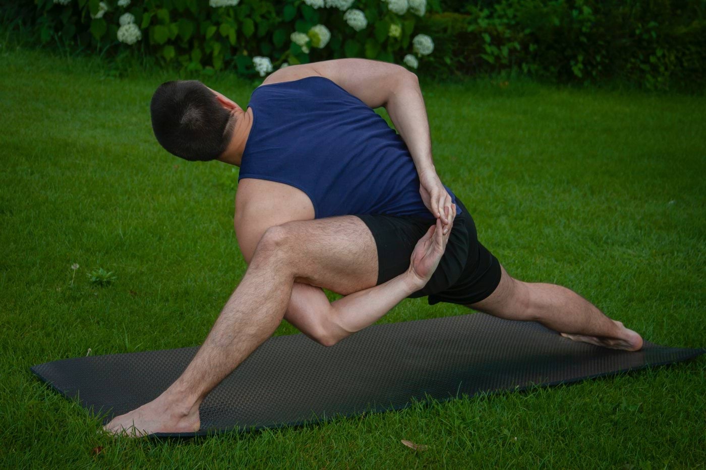 man in blue tank top and black shorts lying on black mat on green grass field