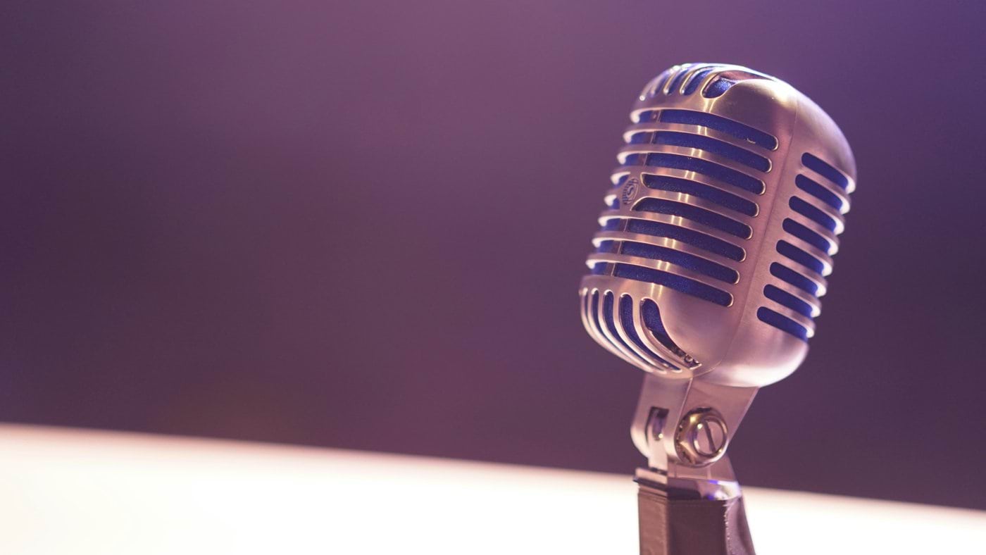 A vintage silver microphone with blue accents against a soft purple background