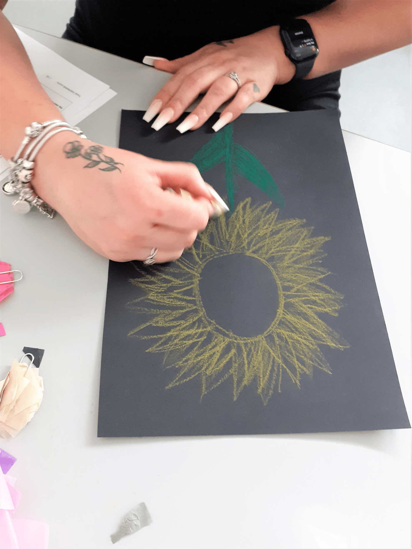 Hands drawing a sunflower on black paper