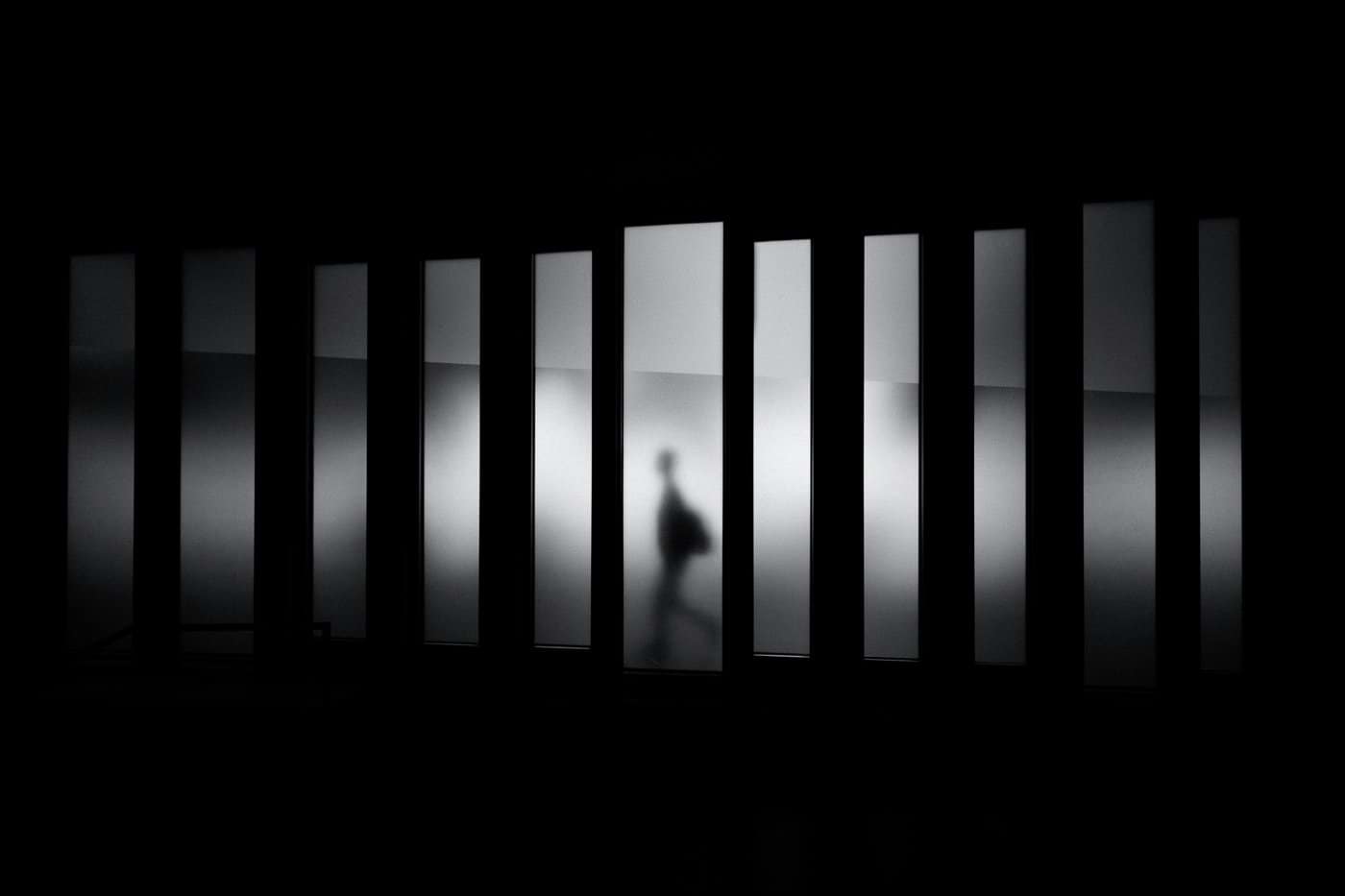 A person in silhouette walking behind a row of vertical frosted glass panels