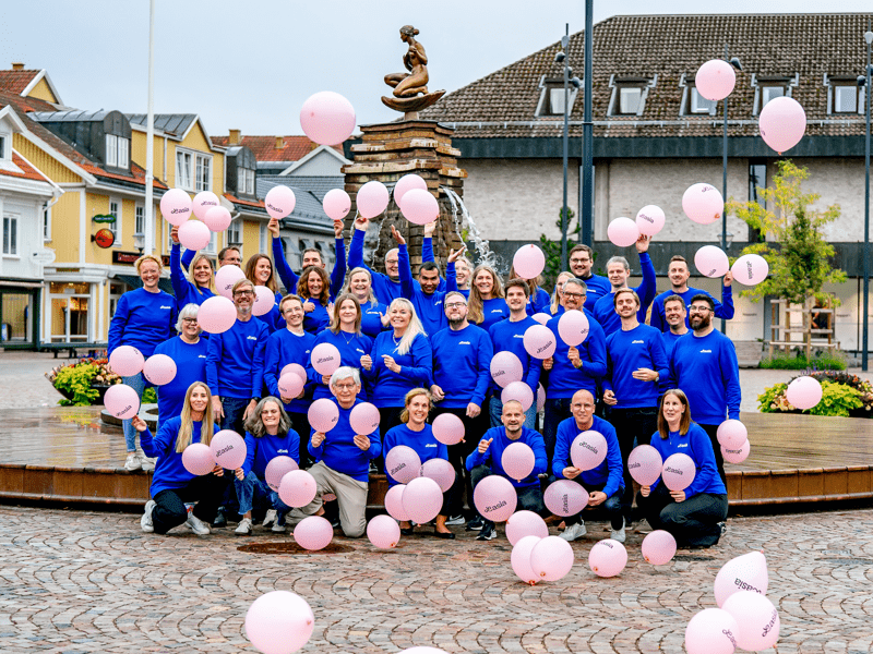 Medarbetare som arbetar på Lasia står med blå tröjor och viftar med rosa ballonger på Falköpings torg.