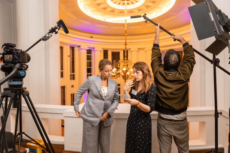 Two women discuss together while a man sets up recording equipment