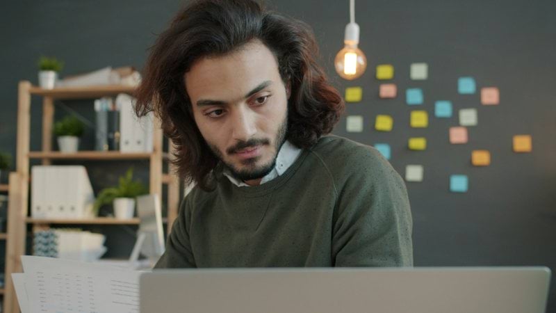 Man with long hair working on laptop in office