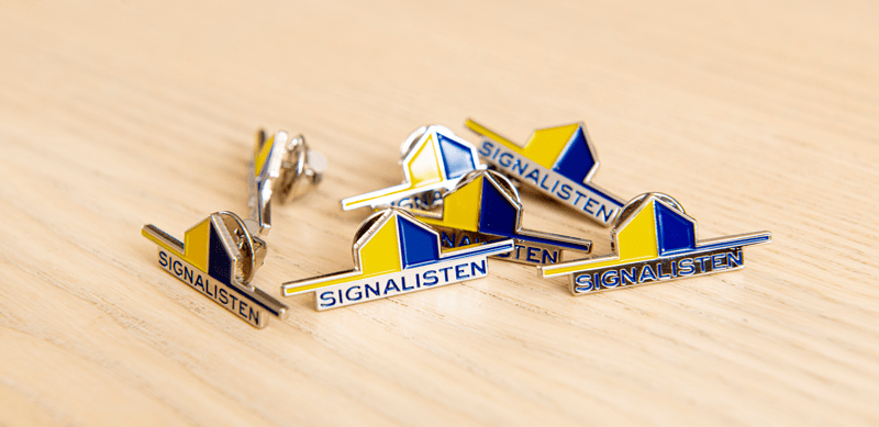 En hög med Signalisten-pins som ligger på ett träbord.